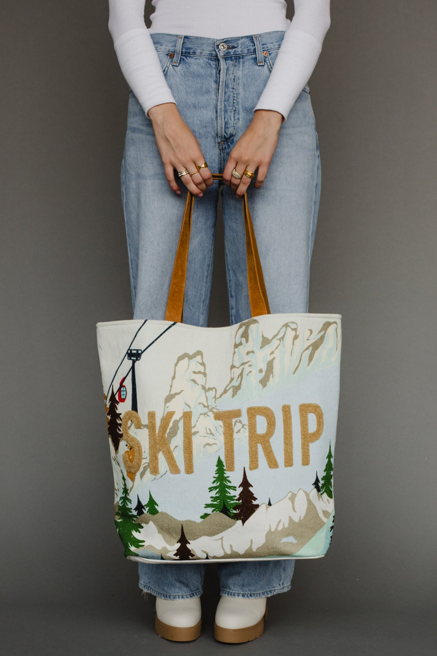 Person holding a tote bag with ' ski trip' design against a gray background