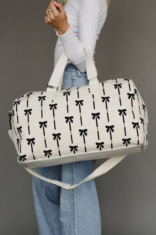 Person holding a white duffel bag with black bow pattern against a gray background
