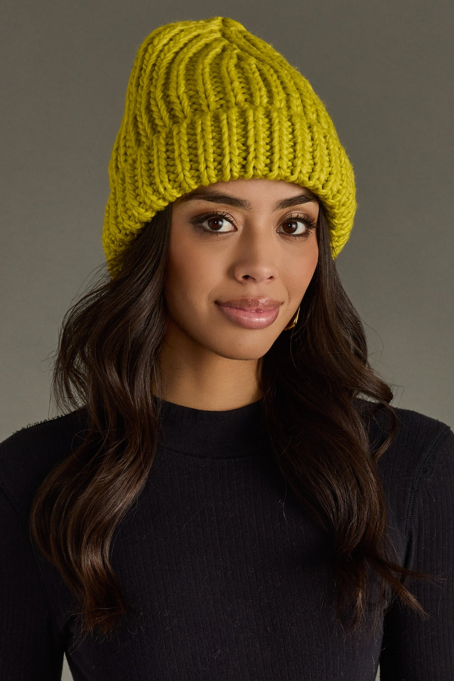 Woman wearing a lime green knit beanie against a gray background