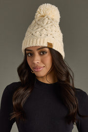 Woman wearing a cream knit beanie with a pom-pom on a gray background