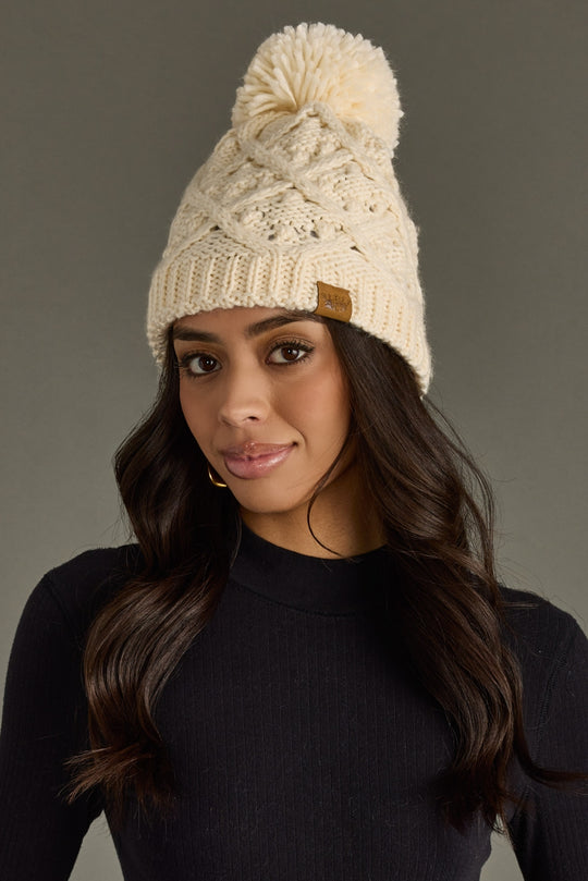Woman wearing a cream knit beanie with a pom-pom on a gray background