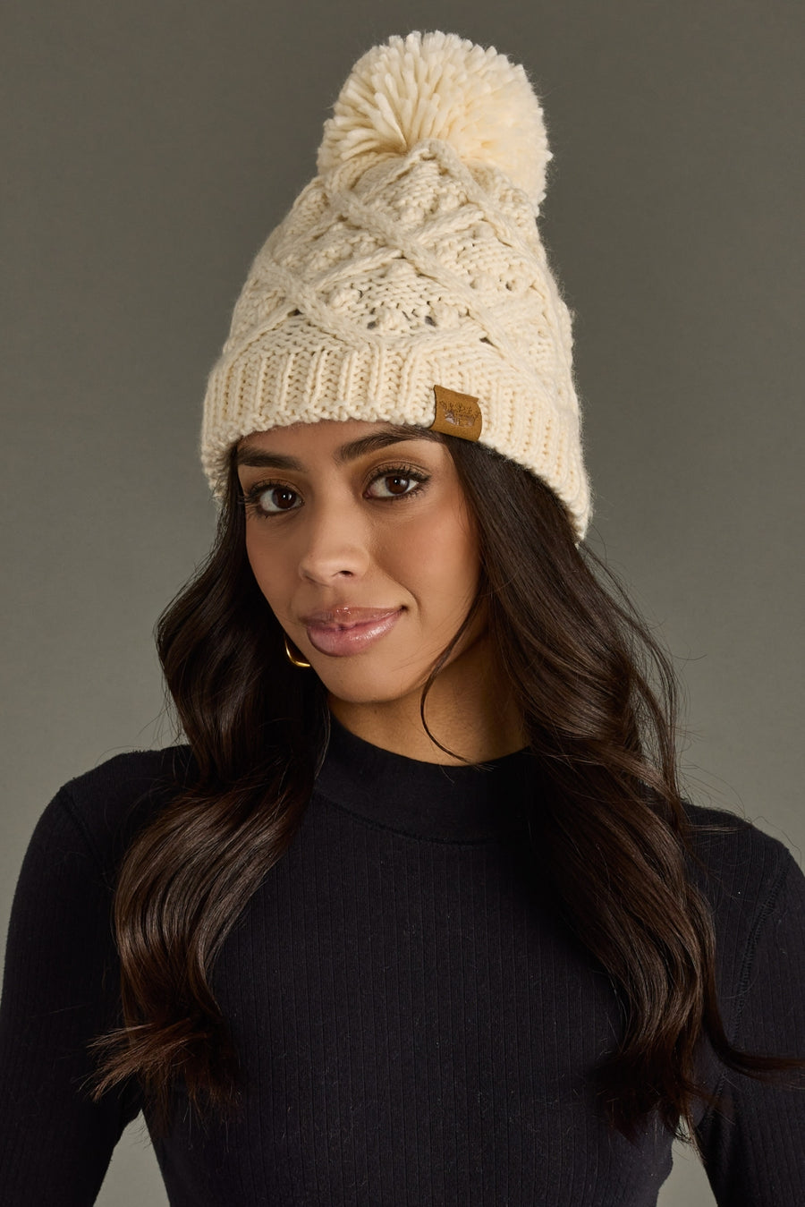 Woman wearing a cream knit beanie with a pom-pom on a gray background