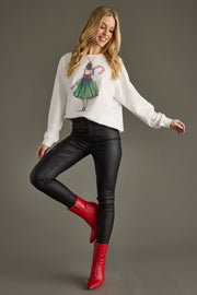 Woman wearing a white sweater with a graphic design, black pants, and red boots on a gray background