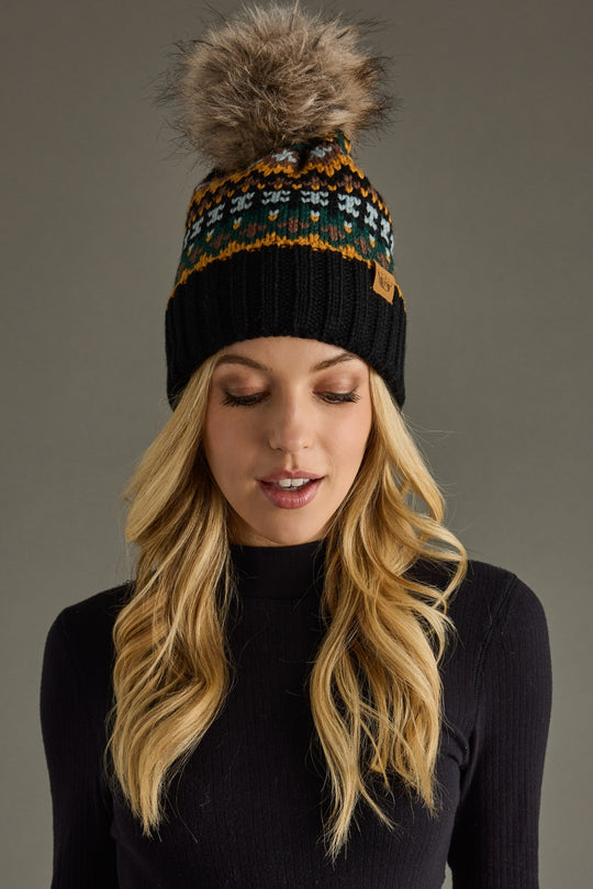 Woman wearing a black knit beanie with a fur pom-pom on a gray background