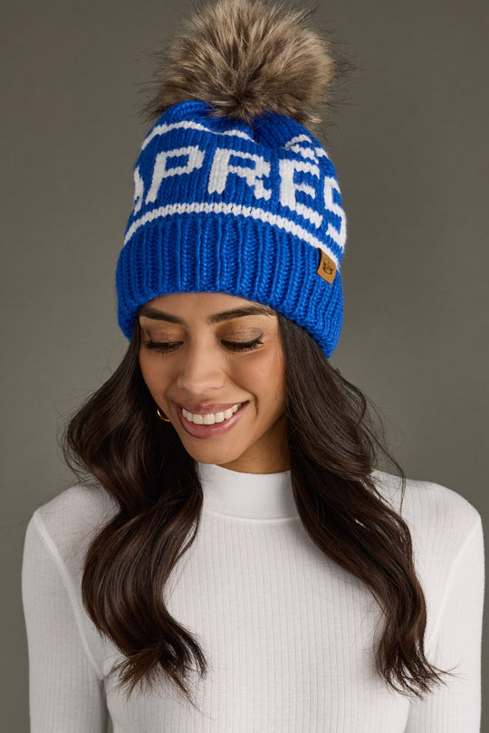 Woman wearing a blue knit beanie with a pom-pom on a gray background