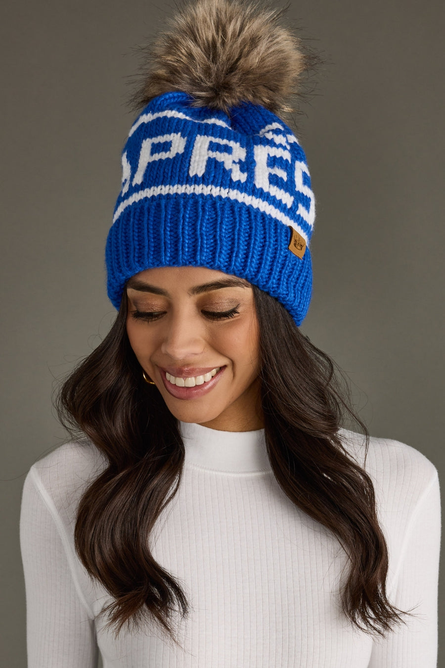 Woman wearing a blue knit beanie with a pom-pom on a gray background