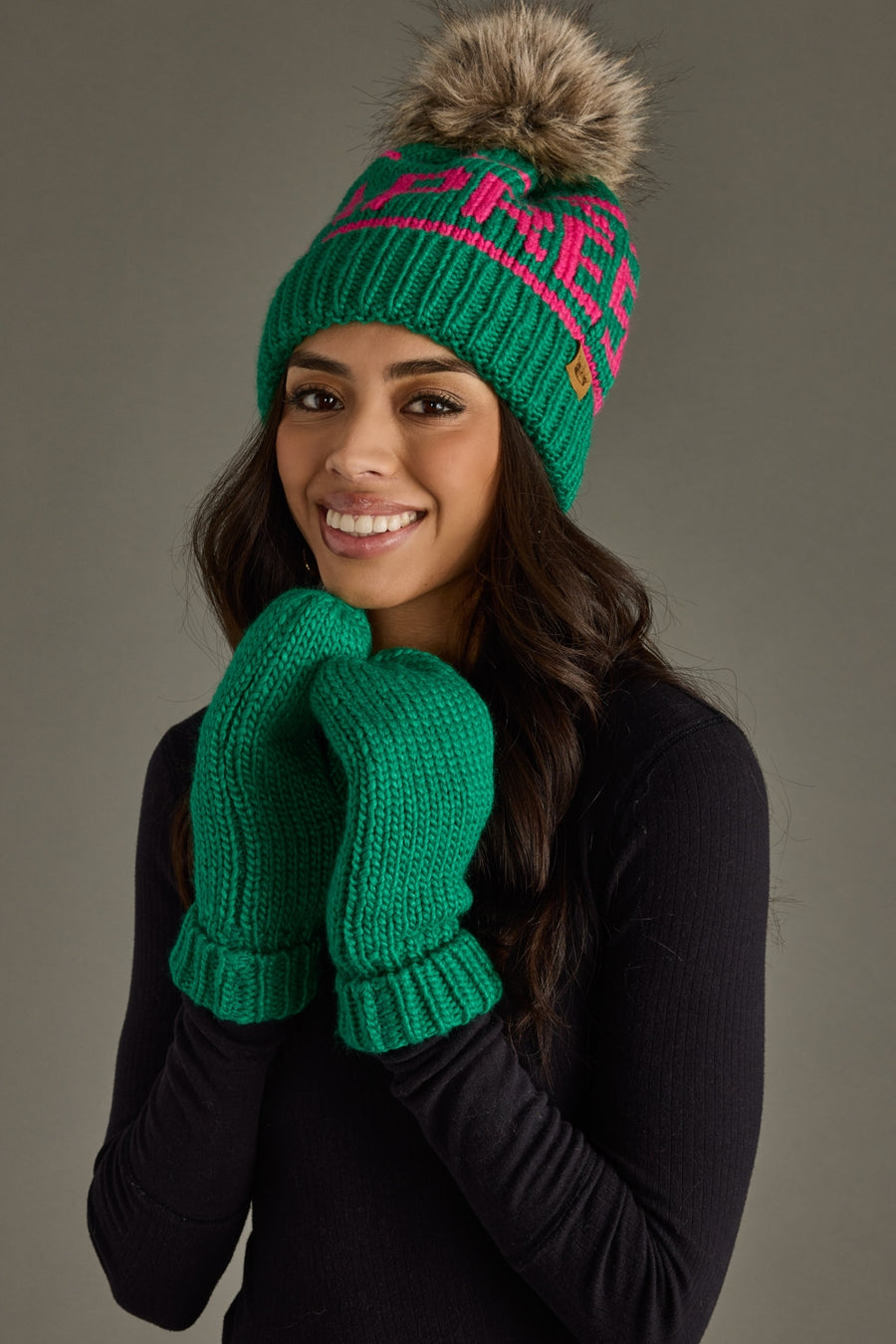 Woman wearing a green knit hat with a pom-pom and matching gloves against a gray background