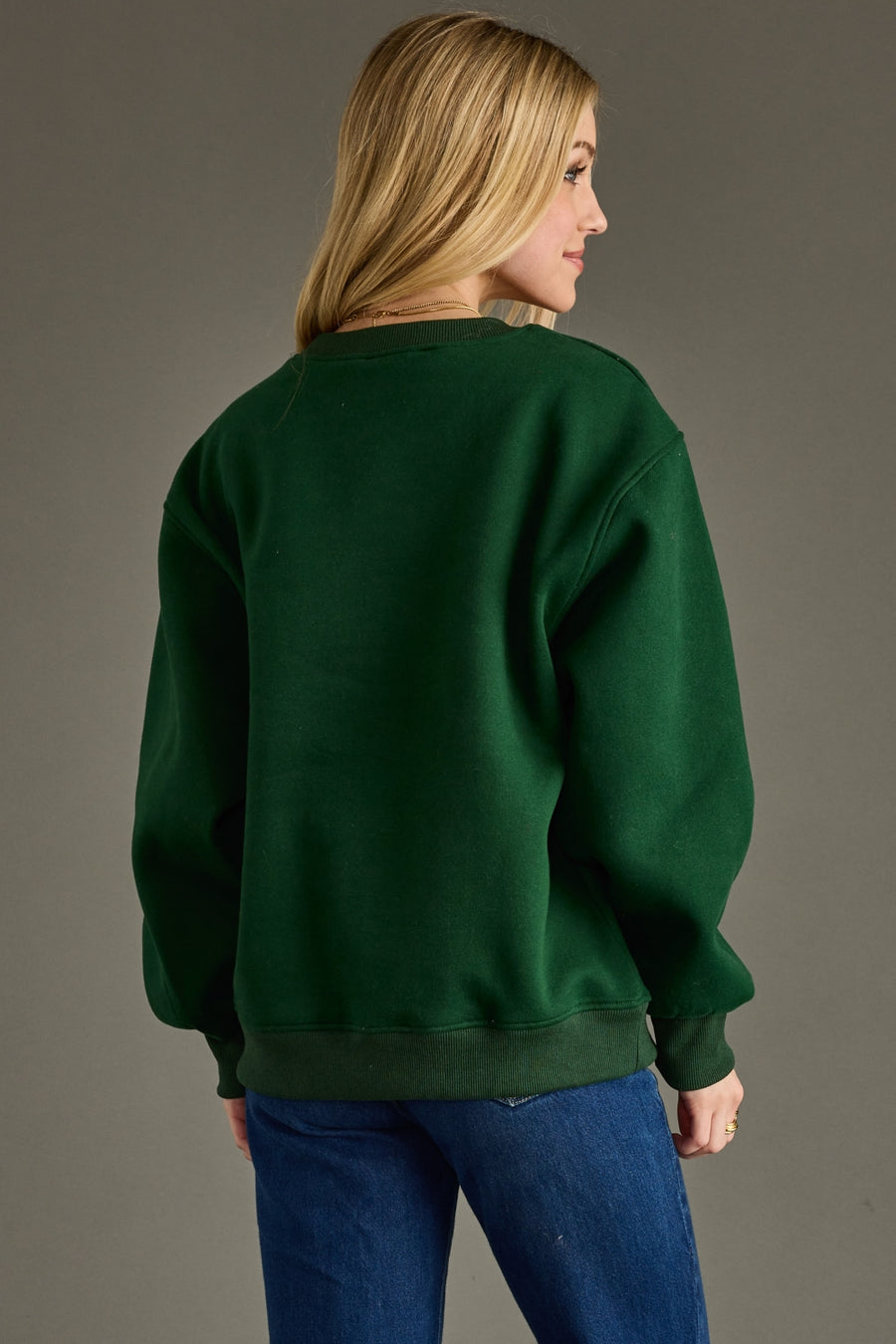Person wearing a green sweatshirt and blue jeans on a gray background