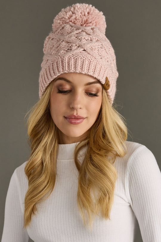 Woman wearing a pink knit beanie with a pom-pom against a gray background