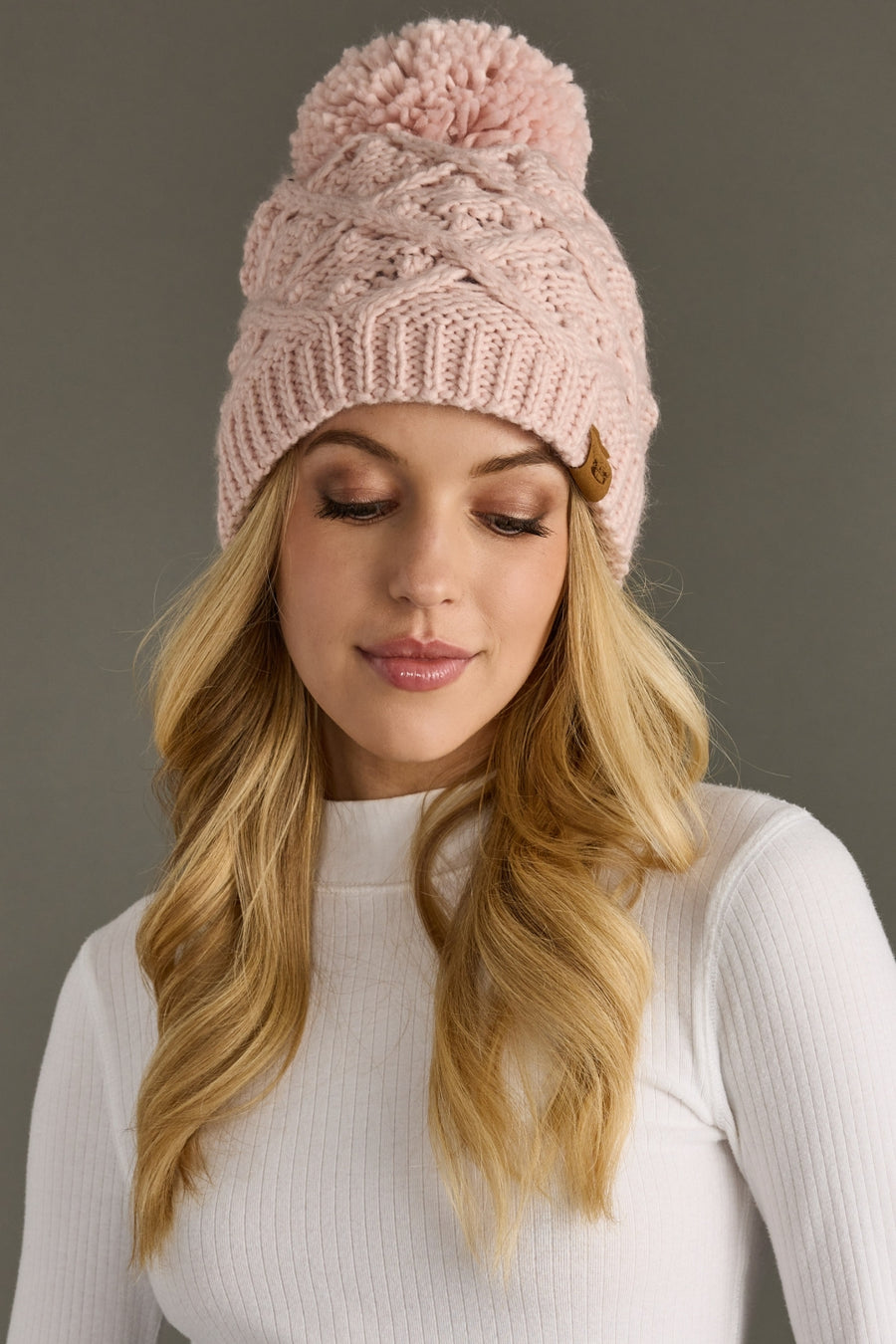 Woman wearing a pink knit beanie with a pom-pom against a gray background