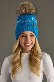 Woman wearing a blue knit beanie with a fur pom-pom on a gray background