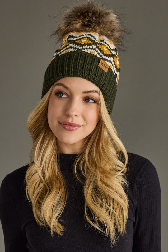Woman wearing a green knit beanie with a pom-pom against a gray background
