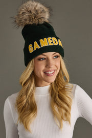 Woman wearing a green beanie with a fur pom-pom and 'GAME DAY' text, against a gray background