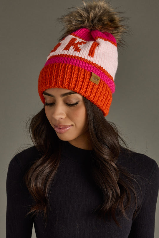 Woman wearing a colorful knit beanie with a pom-pom on a gray background