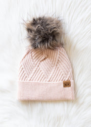Pink knit beanie with fur pom-pom on a white background