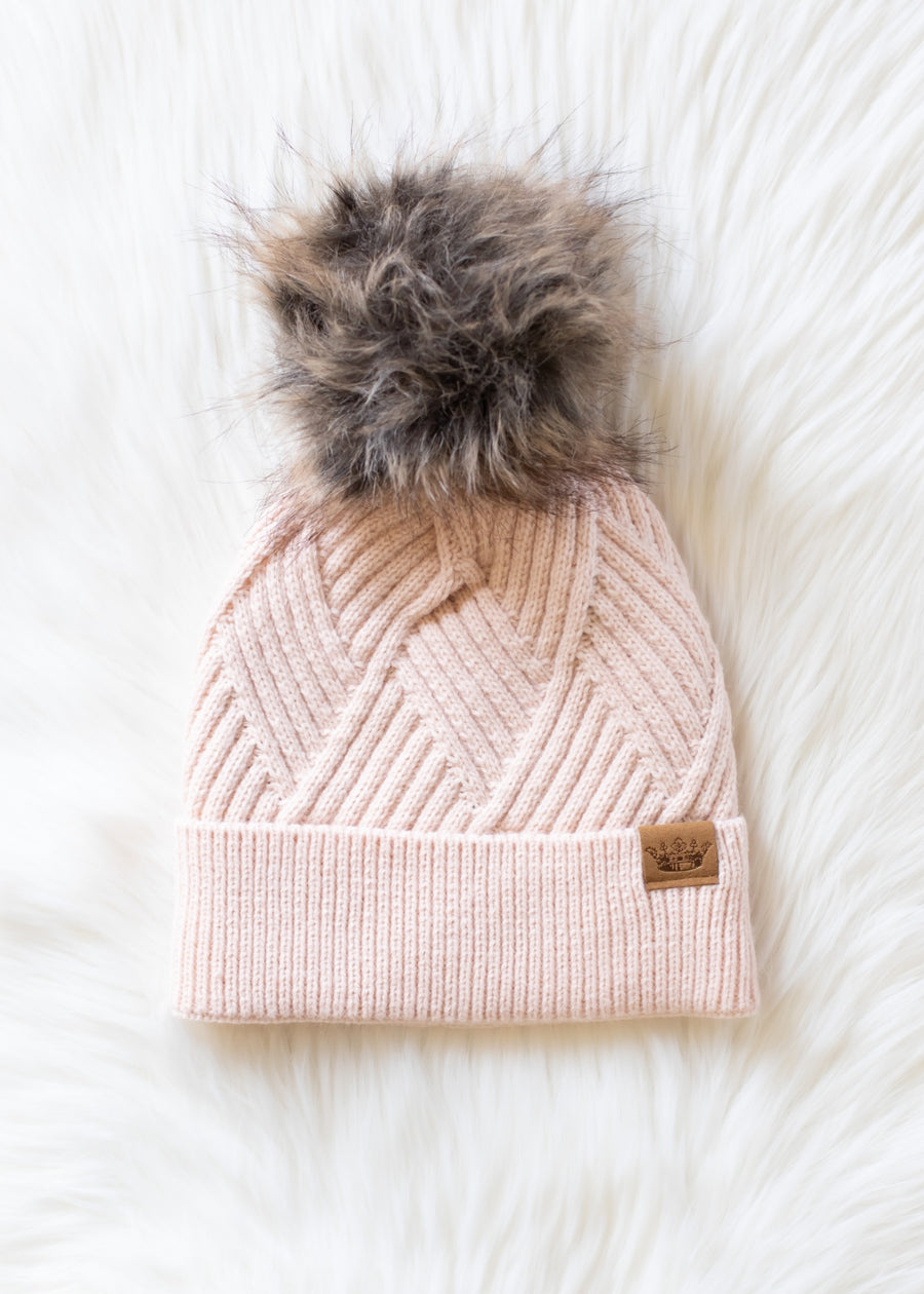 Pink knit beanie with fur pom-pom on a white background