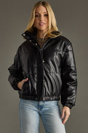 Woman wearing a black leather jacket and light blue jeans against a gray background