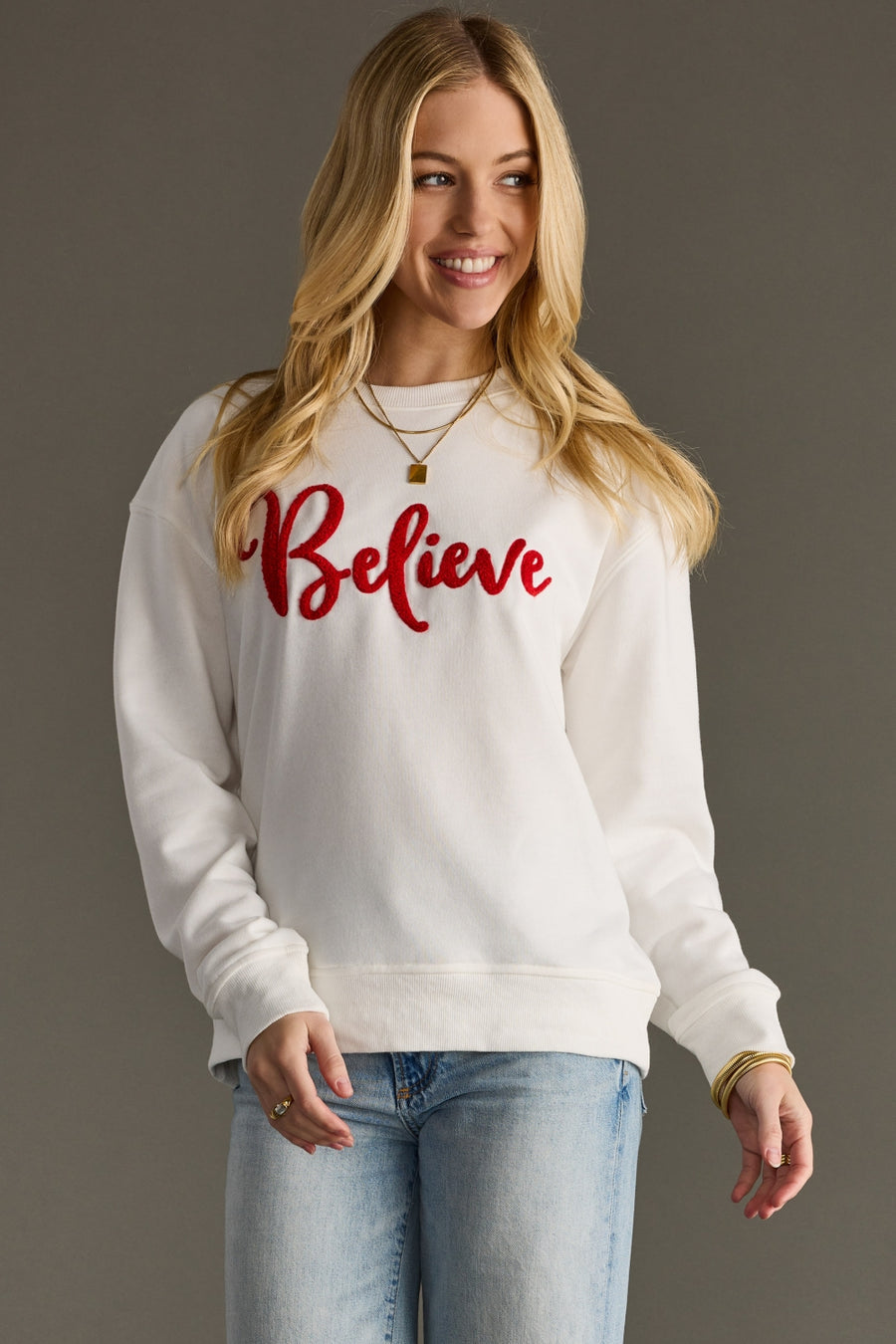 Woman wearing a white sweatshirt with 'Believe' in red text on a gray background