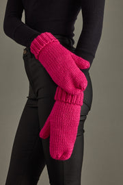 Person wearing bright pink knitted mittens against a neutral background
