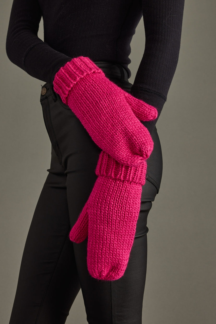 Person wearing bright pink knitted mittens against a neutral background