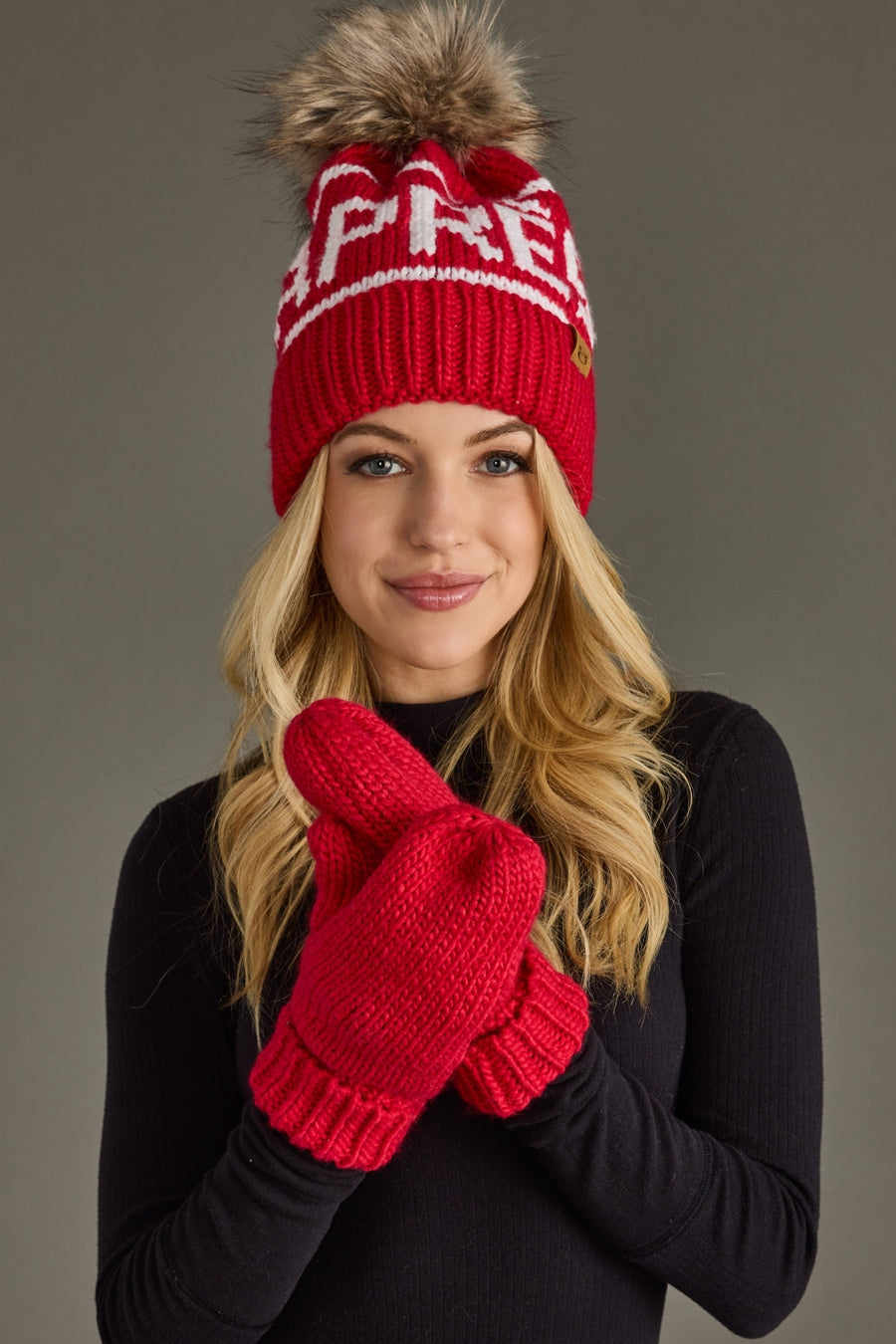 Person wearing a red knit hat with a pom-pom and matching gloves on a gray background