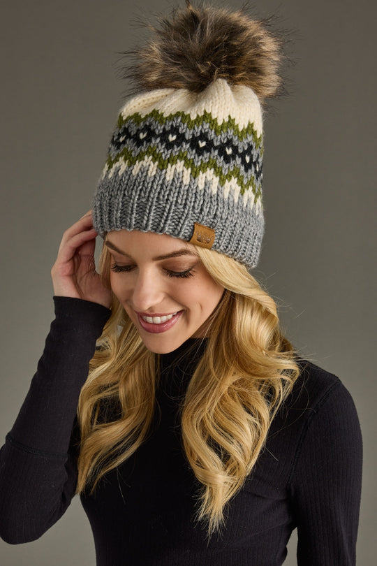 Woman wearing a patterned knit hat with a pom-pom against a gray background