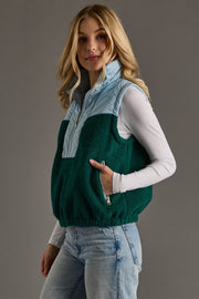 Woman wearing a green and light blue vest against a gray background