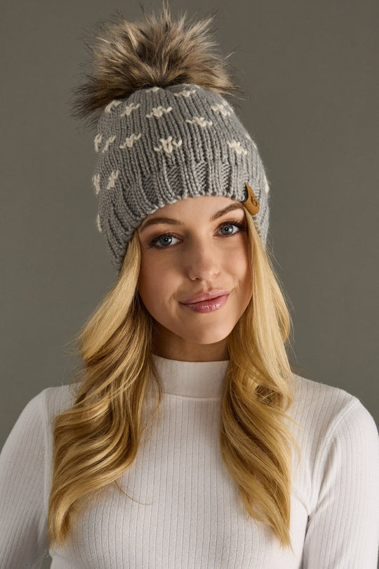 Woman wearing a gray knit beanie with a pom-pom against a neutral background
