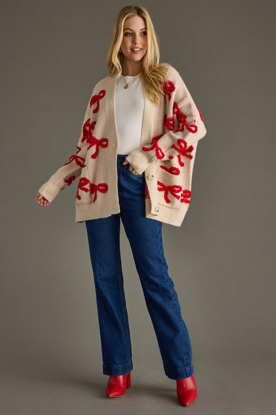 Woman wearing a beige cardigan with red patterns, white shirt, blue jeans, and red shoes on a gray background
