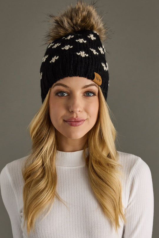 Woman wearing a black beanie with a fur pom-pom on a gray background