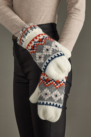 Pair of knit mittens with a pattern held by a person against a neutral background