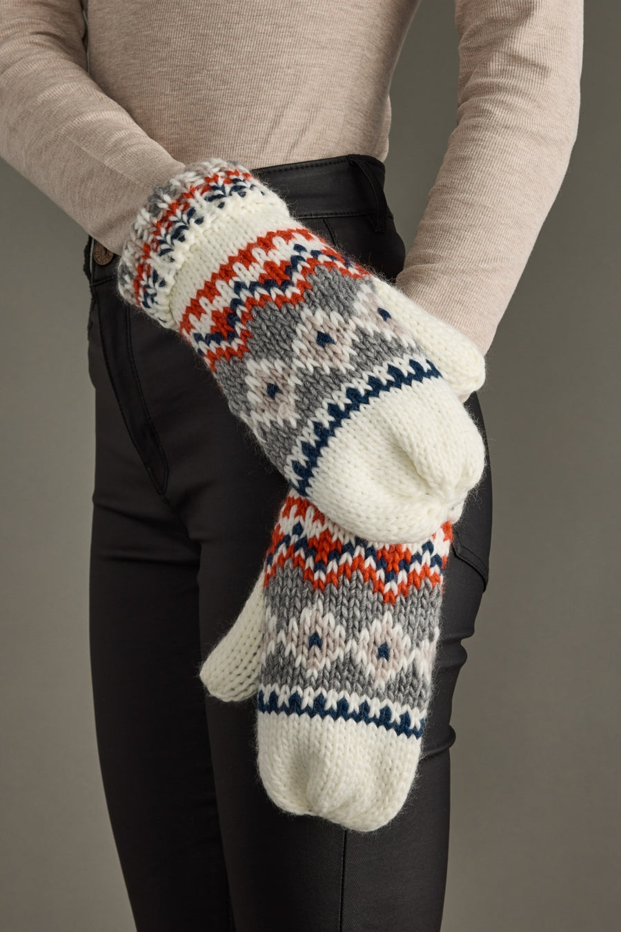 Pair of knit mittens with a pattern held by a person against a neutral background