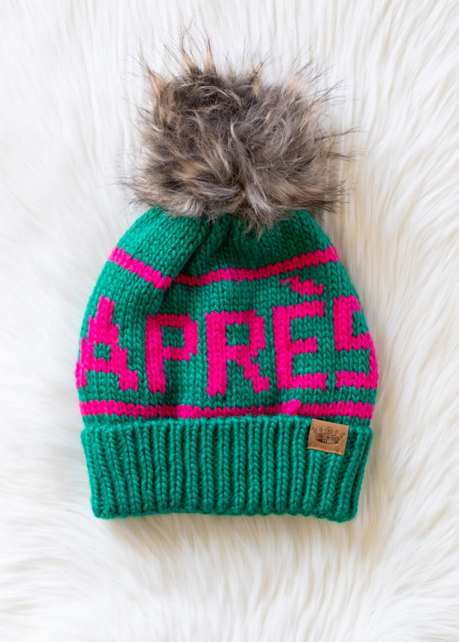 Green knit beanie with pink text and fur pom-pom on a white background