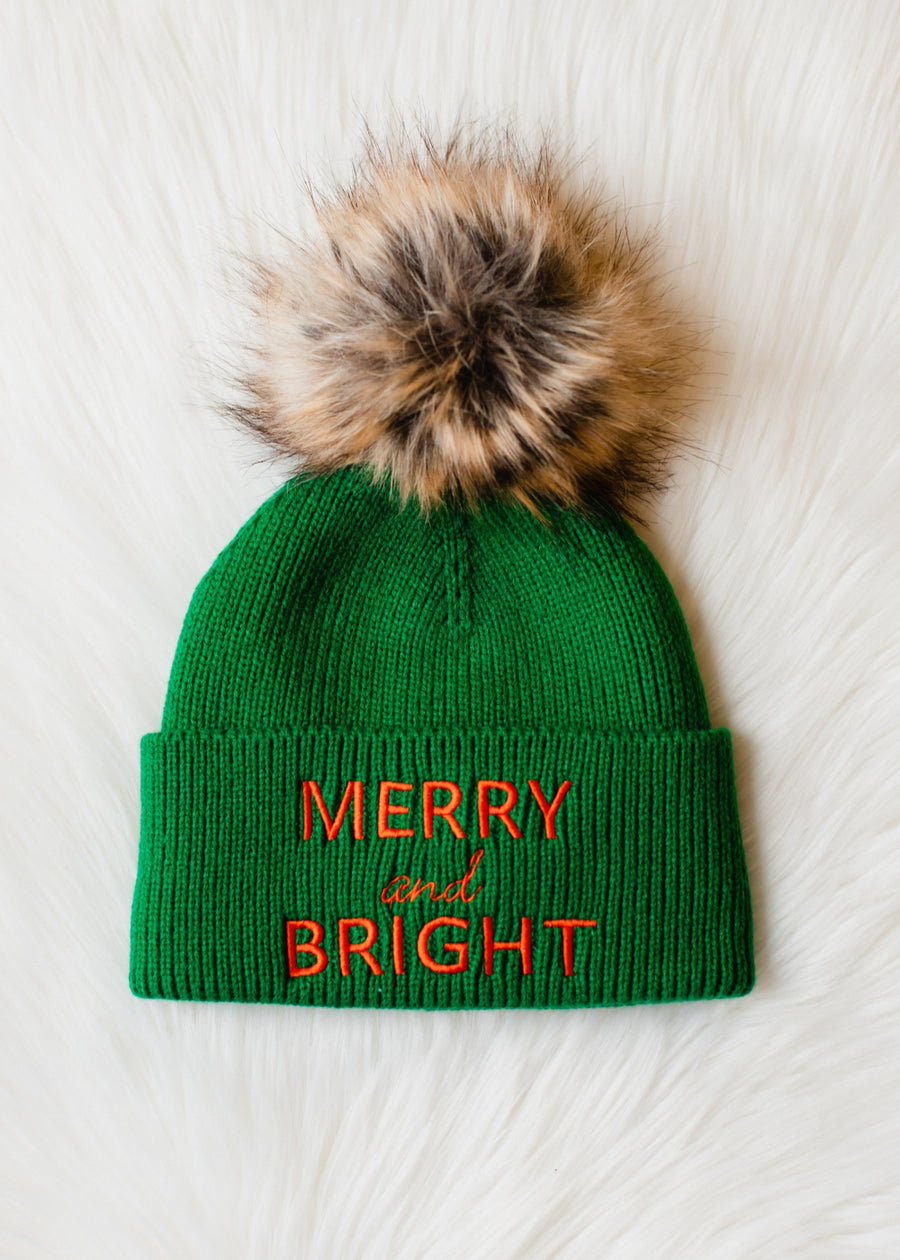 Green beanie with fur pom-pom and 'Merry and Bright' text on a white background