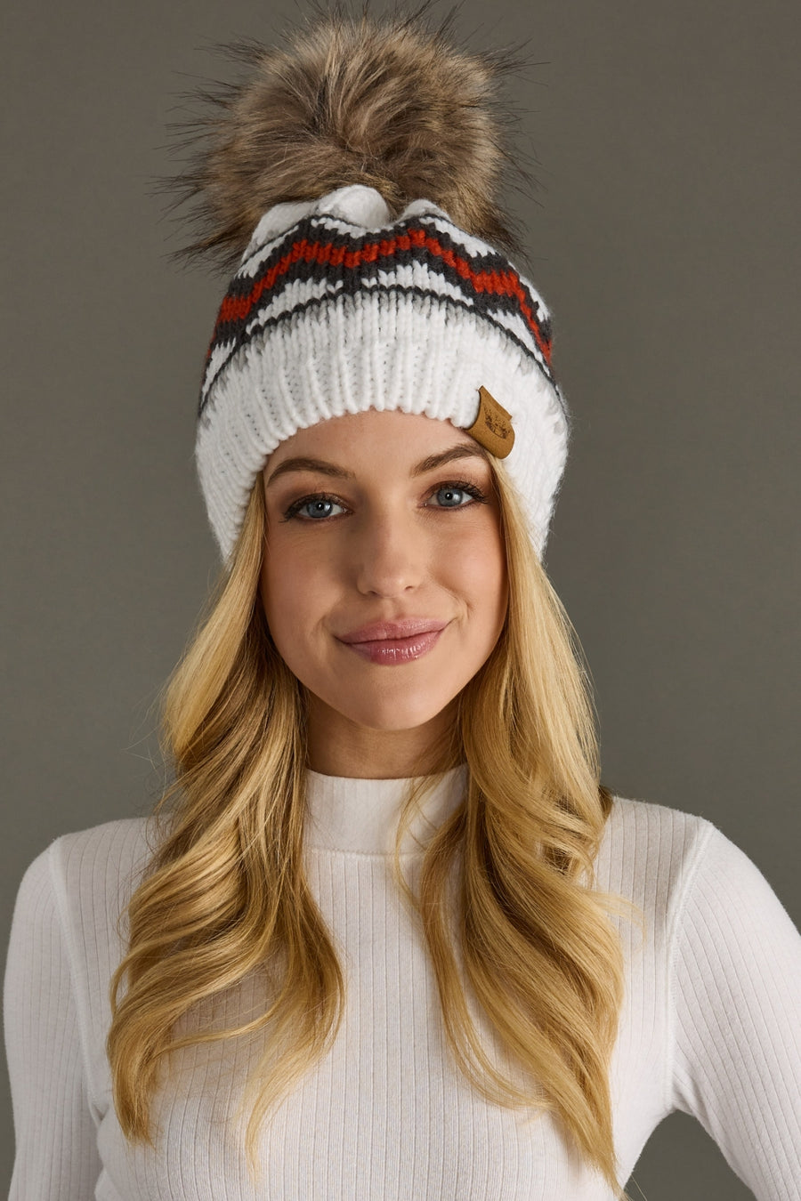 Woman wearing a white knit beanie with a pom-pom on a gray background
