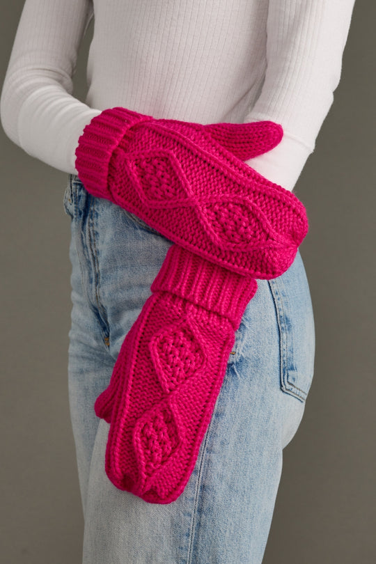 Person wearing bright pink knitted mittens with a pattern on a neutral background