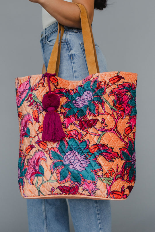 Colorful floral tote bag with a tassel held by a person wearing jeans against a gray background