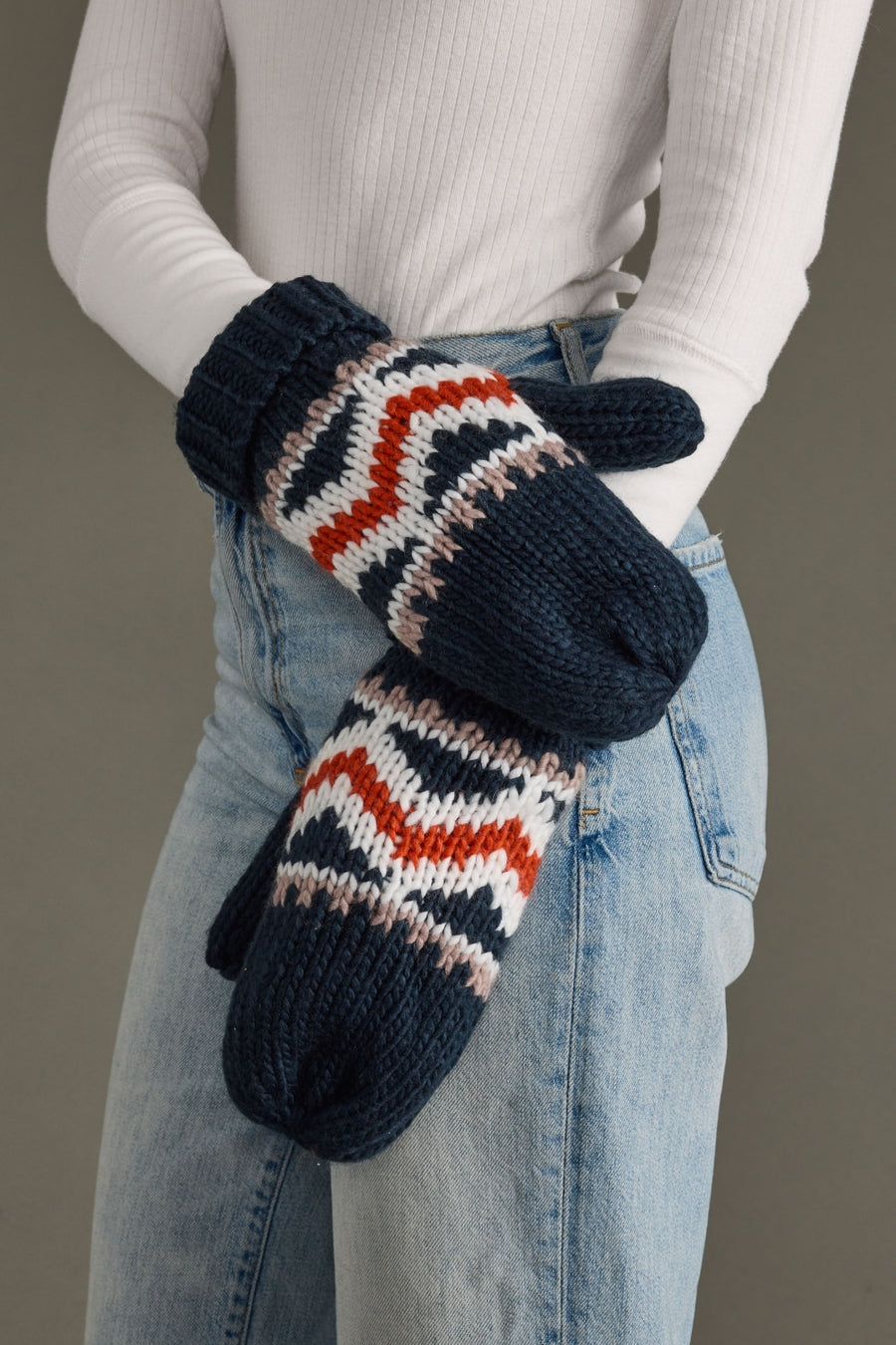 Person wearing navy and patterned mittens with a neutral background