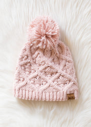 Pink knitted beanie with a pom-pom on a white fluffy surface