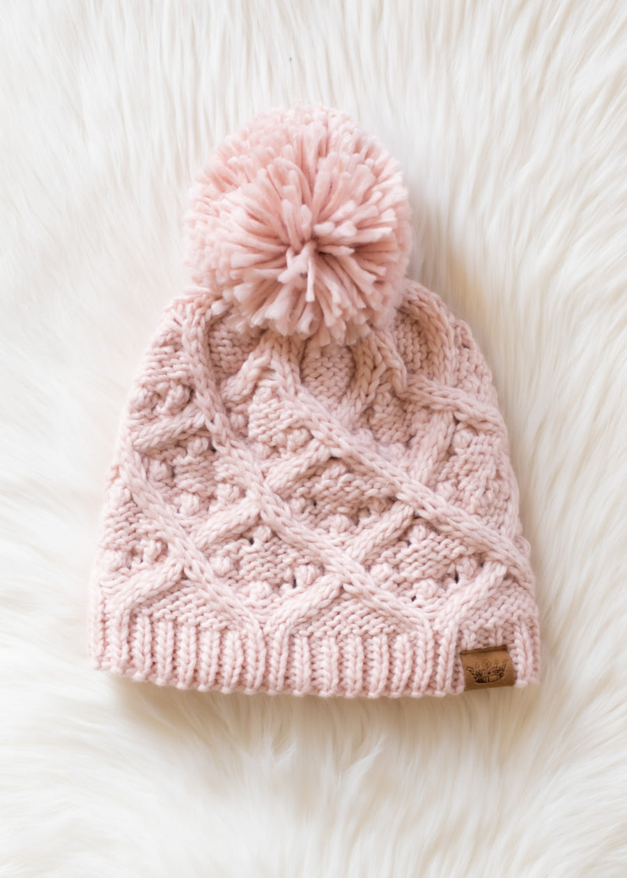 Pink knitted beanie with a pom-pom on a white fluffy surface