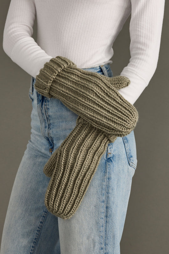 Person wearing green knitted mittens with a plain background