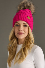 Woman wearing a bright pink knit beanie with a fur pom-pom on a gray background