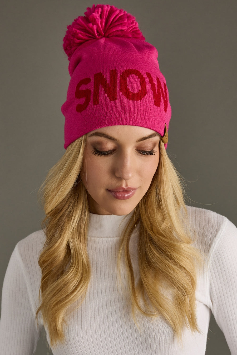 Woman wearing a pink beanie with 'SNOW' text on a gray background