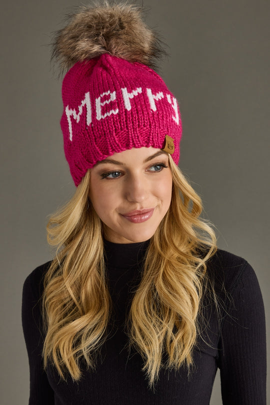 Woman wearing a pink knit hat with a fur pom-pom and 'Merry' text on a gray background