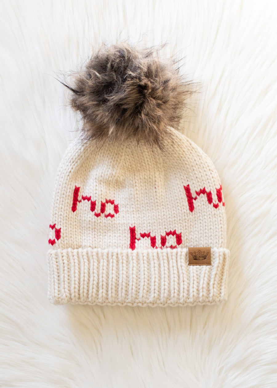 Knitted beanie with red text and fur pom-pom on a white background
