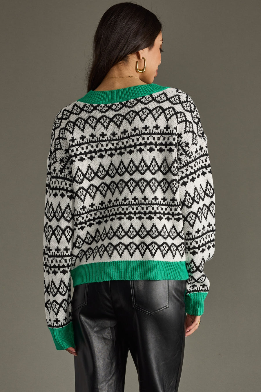 Person wearing a patterned sweater with green trim on a gray background