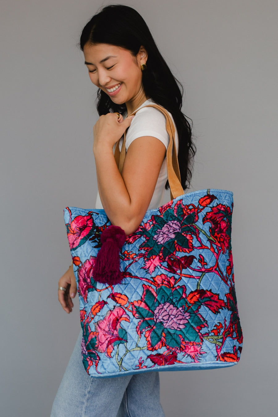 Woman holding a colorful floral tote bag against a gray background