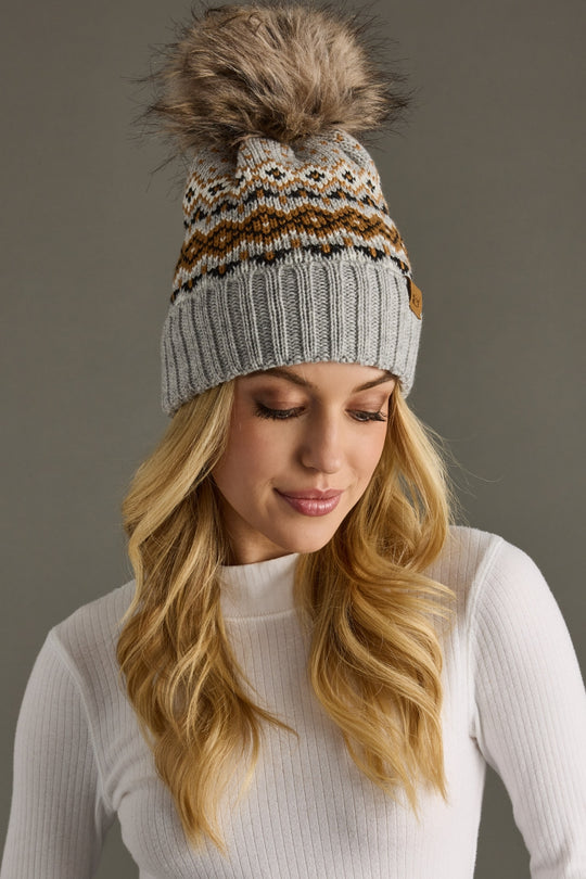 Woman wearing a patterned knit beanie with a pom-pom on a gray background