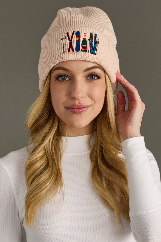 Woman wearing a blush beanie with embroidered designs on a gray background