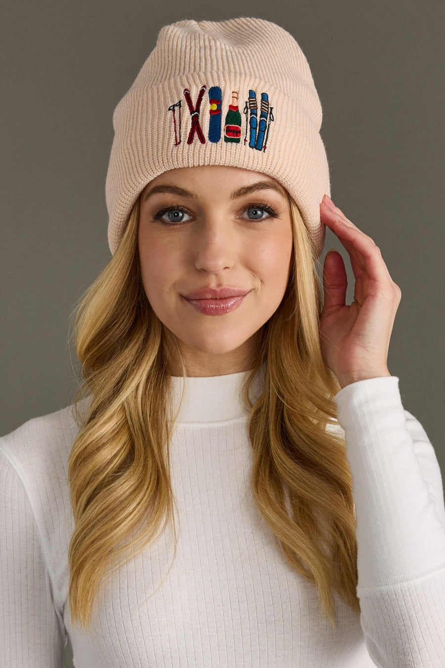 Woman wearing a blush beanie with embroidered designs on a gray background